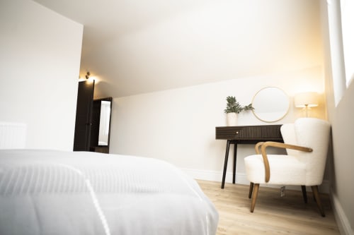 Modern bedroom at Stay at Wellington Circus in Nottingham with white bed, desk, round mirror, and cream chair in The Oriel