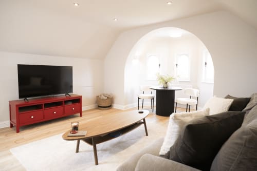 The Oriel Loft lounge at Stay Wellington Circus with red TV stand, black sectional sofa, wooden coffee table, and arched