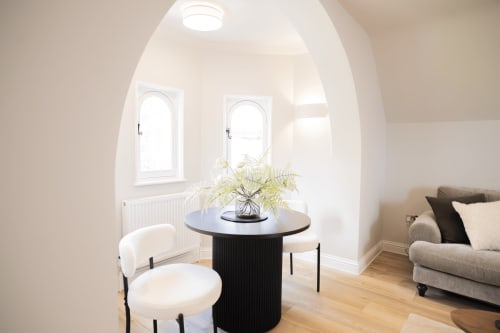Bright Oriel Loft apartment in Nottingham with arched windows, modern round black table, cream chair, and beige sofa