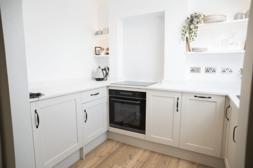 Modern white kitchen in The Oriel Loft apartment at Stay at Wellington Circus, Nottingham, featuring built-in oven, shelving,
