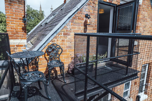 Rooftop terrace at The Oriel Loft in Nottingham with ornate black chairs, mesh railing, and brick building architecture