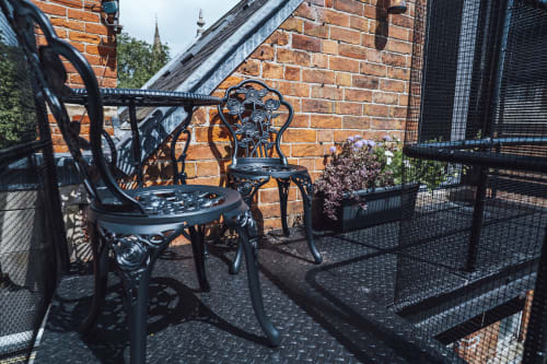 Black ornate chairs on metal balcony of The Oriel Loft apartment in Nottingham, brick building backdrop