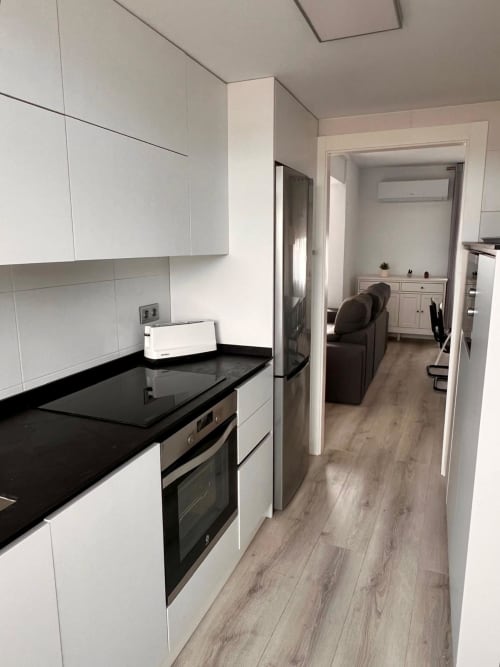 Cocina moderna blanca con encimeras negras en apartamento CASA GIL, Águilas España con vista a la sala de estar