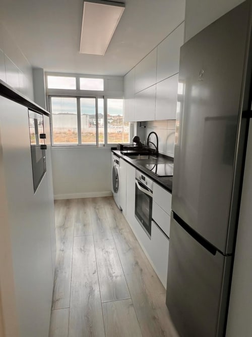 Cocina moderna blanca con electrodomésticos de acero inoxidable, lavadora y vistas al mar en apartamento Casa Gil, Águilas
