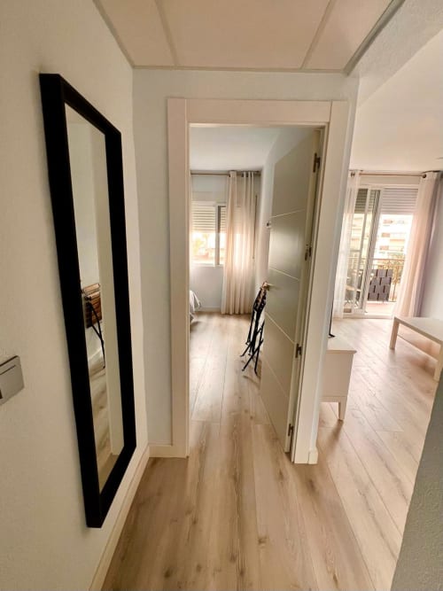 Pasillo moderno de apartamento en Casa Gil, Águilas con suelo de madera clara, puertas blancas, espejo con marco negro y vistas al mar