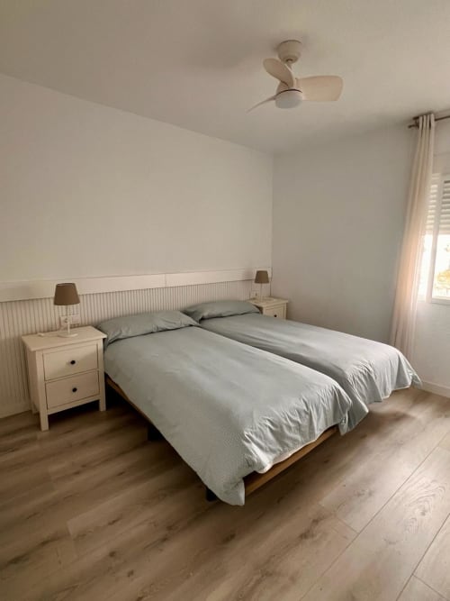 Dormitorio moderno en apartamento Casa Gil, Águilas con cama doble, mesitas blancas, ventilador de techo y piso de madera