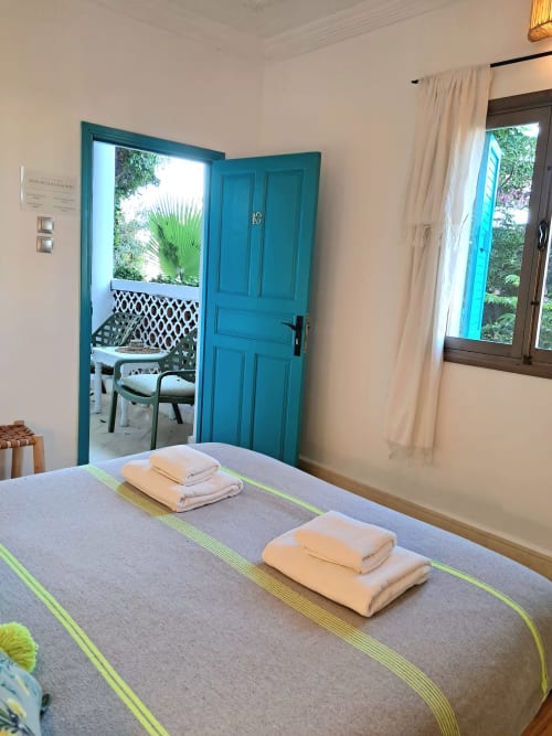 Bedroom at Vent Des Dunes & Spa in Essaouira with turquoise door, folded towels, and garden view balcon access