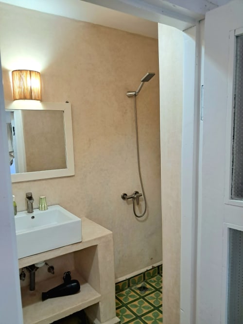Modern bathroom at Vent Des Dunes & Spa with white sink, mirror, hand shower, and traditional green tile flooring in