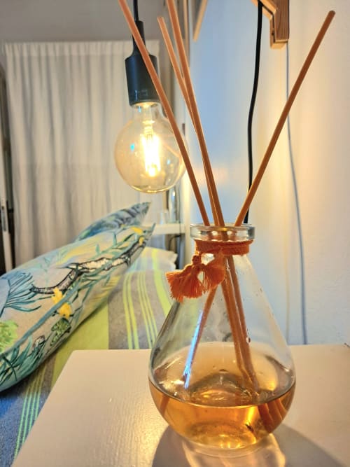 Reed diffuser with amber liquid and wooden sticks beside decorative fish pillow in Vent Des Dunes hotel room, Essaouira