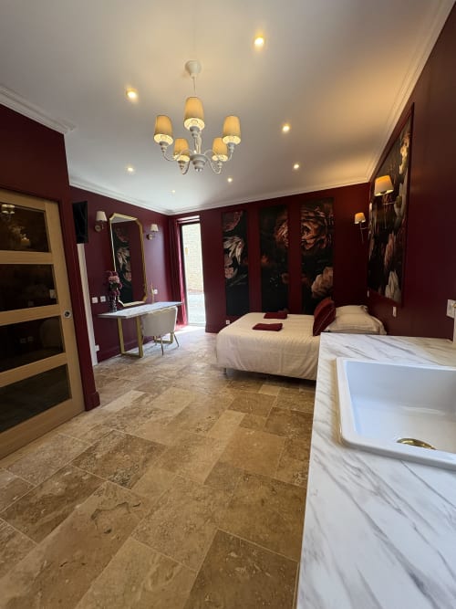 Chambre luxueuse aux murs bordeaux, baignoire en marbre et lustre élégant au Domaine Des Hêtres
