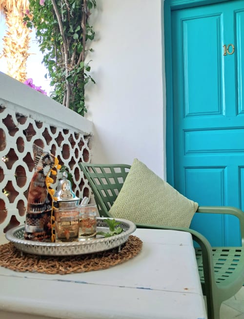 Turquoise door and green chair on balcony at Vent Des Dunes hotel in Essaouira with garden view