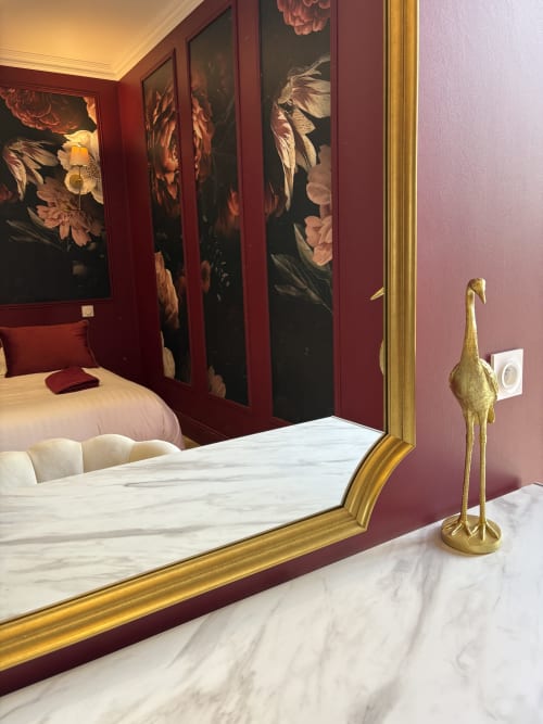 Miroir de luxe à cadre doré, sol en marbre, murs bordeaux et œuvres florales à Domaine Des Hêtres