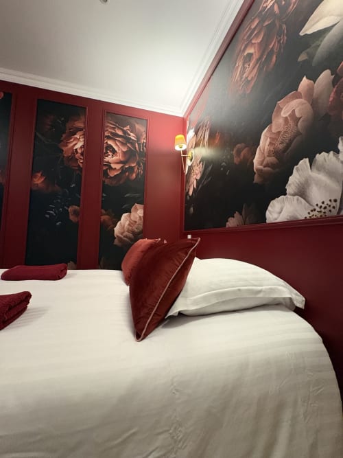 Chambre luxueuse aux murs bordeaux, œuvres florales, literie blanche et coussins en velours rouge à Domaine Des Hêtres