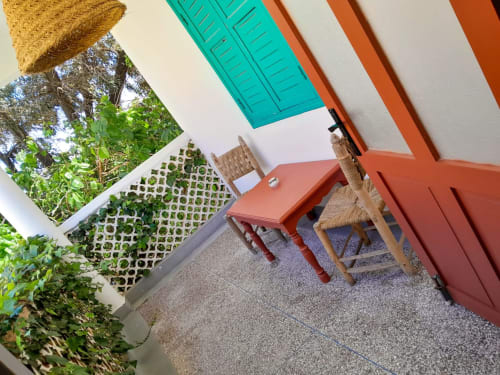 Balcony terrace at Vent Des Dunes & Spa, Essaouira with red table, wicker chair, turquoise shutters, and lush greenery views