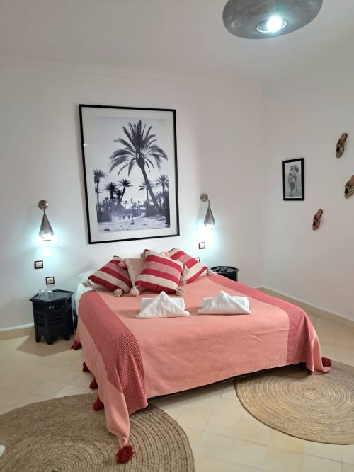 Elegant bedroom at Vent Des Dunes & Spa in Essaouira with coral bedding, palm tree artwork, and ambient lighting