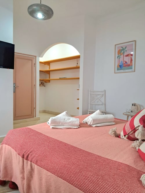 Spacious hotel bedroom at Vent Des Dunes in Essaouira with pink bedding, walk-in closet, and modern amenities