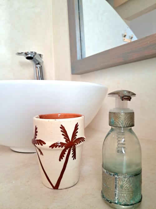 Bathroom vanity at Vent Des Dunes & Spa with decorative ceramic cup and soap dispenser near sink and mirror