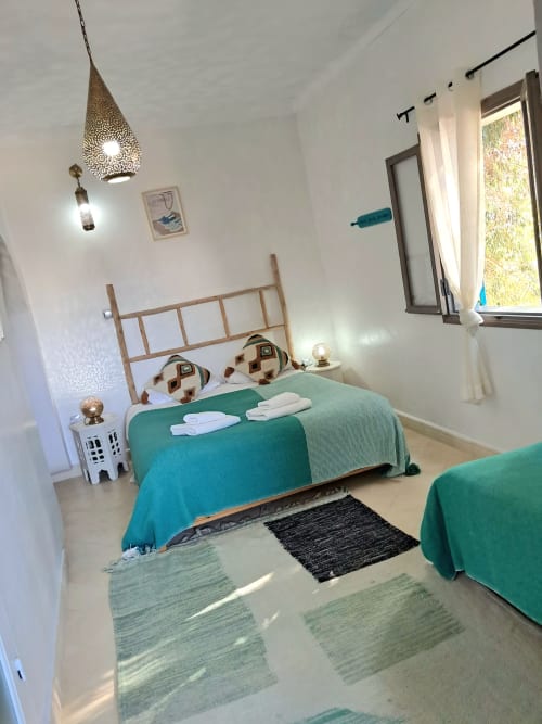 Bright bedroom at Vent Des Dunes Essaouira with turquoise beds, wooden headboard, Moroccan decor, and garden views from