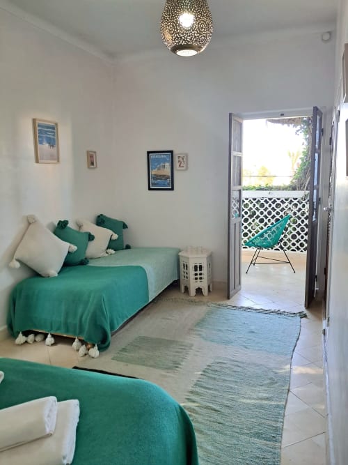 Bright bedroom at Vent Des Dunes in Essaouira with twin beds, green bedding, balcony access, and garden view