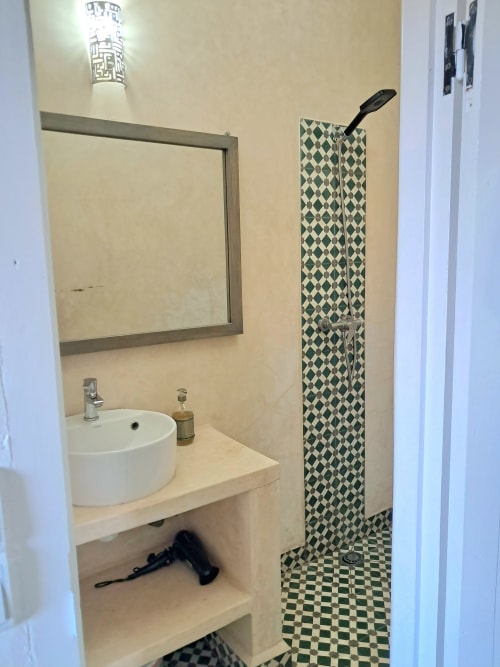 Modern bathroom at Vent Des Dunes with round sink, mirror, and green diamond-patterned shower area in Essaouira