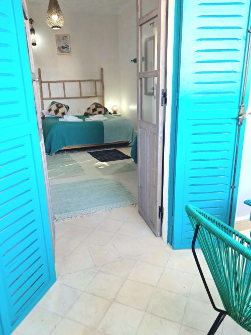 Bright bedroom at Vent Des Dunes & Spa in Essaouira with turquoise doors, metal bed frame, and tiled floor