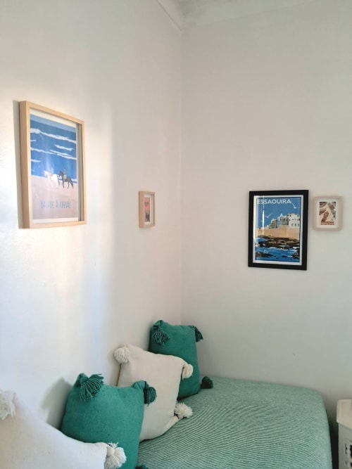 Cozy bedroom at Vent Des Dunes hotel in Essaouira with green cushions and travel posters on white walls