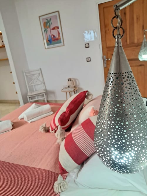 Chambre d'hôtel bord de mer avec suspension en métal perforé, linge de lit rose et coussins rouges au Vent Des Dunes & Spa