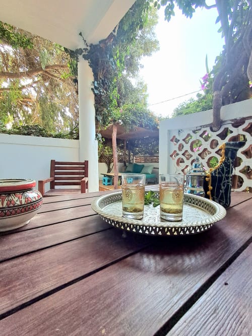 Outdoor terrace at Vent Des Dunes & Spa in Essaouira with drinks, wooden bench, ivy-covered walls, and garden seating area