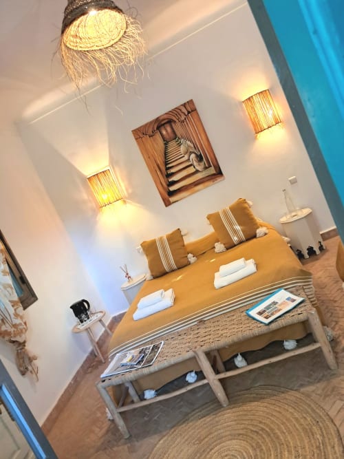 Luxury bedroom at Vent Des Dunes & Spa in Essaouira with ochre bedding, woven pendant lamp, and warm wall sconces