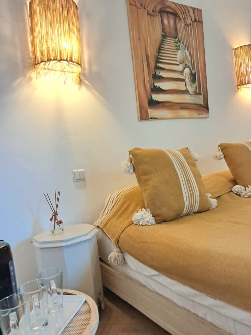 Cozy hotel room at Vent Des Dunes in Essaouira with mustard-gold bedding, decorative pillows, wall sconces, and framed