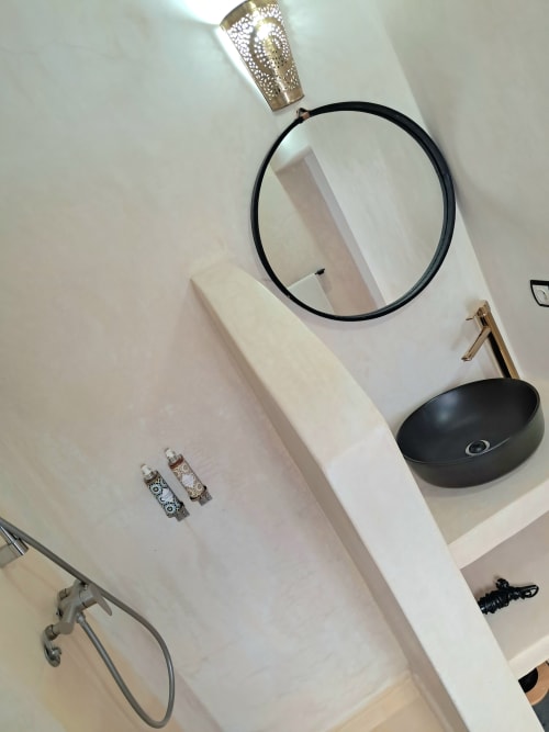 Modern bathroom vanity at Vent Des Dunes & Spa in Essaouira with circular mirror, black vessel sink, and decorative brass