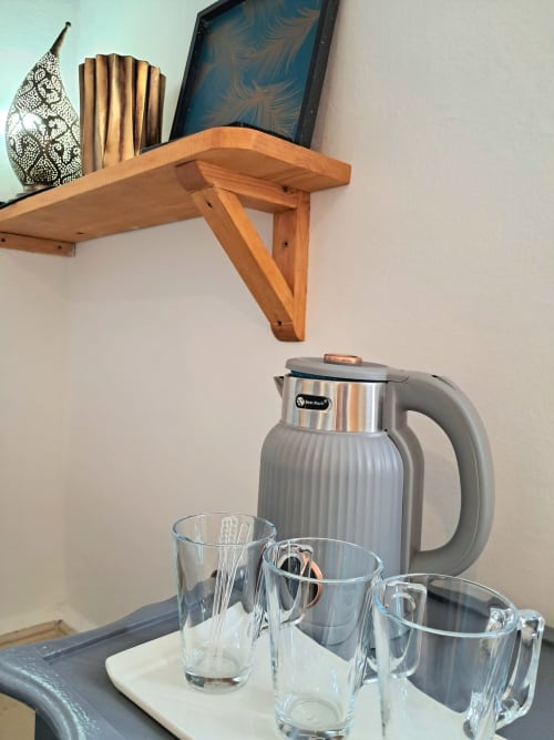Wooden shelf with decorative items and gray thermal kettle with glasses at Vent Des Dunes hotel, Essaouira