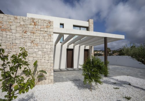 Villa moderna en Calp con fachada de piedra, entrada con pérgola blanca y piscina privada rodeada de jardines mediterráneos