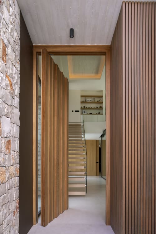 Entrada moderna en madera con puerta abierta hacia escalera y estanterías en Villa Ona en Riurau Home, Calp