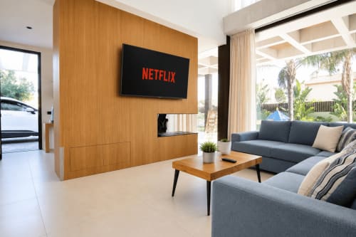 Sala de estar moderna en villa de Riurau Home en Calp con Netflix en TV pantalla plana, sofás grises, pared de madera y vistas a la piscina