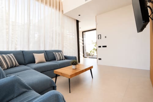 Sala de estar de villa moderna en Riurau Home Calp con sofá azul, mesa de madera y vistas al mar a través de grandes ventanales