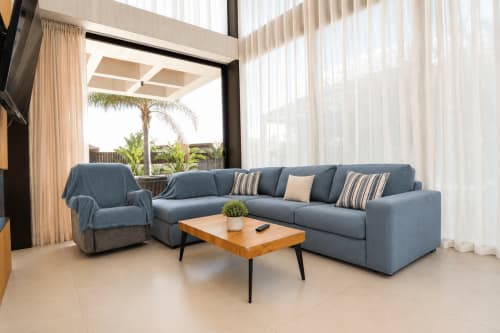 Salón moderno en Villa Ona de Riurau Home, Calp, con sofá seccional azul, mesa de café de madera y vistas al jardín tropical