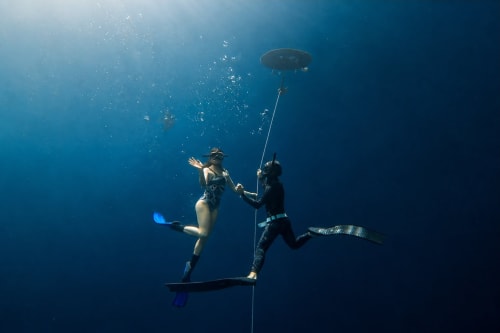 Dos buceadores explorando un cenote subacuático cerca de Valladolid, Yucatán con cuerda y equipo en agua azul