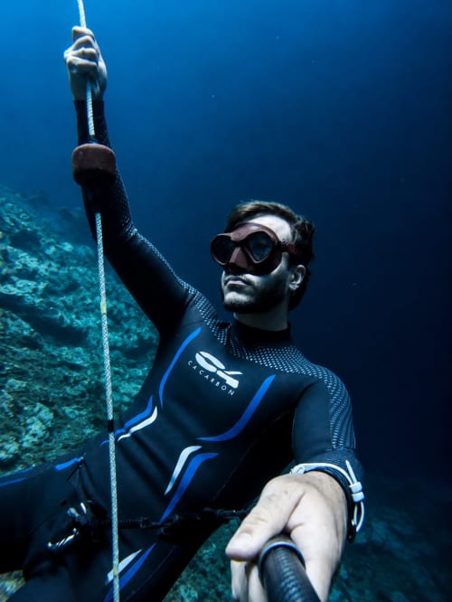 Buzo en traje de neopreno negro sujetando cuerda bajo el agua cerca del arrecife de coral en cenote de Yucatán