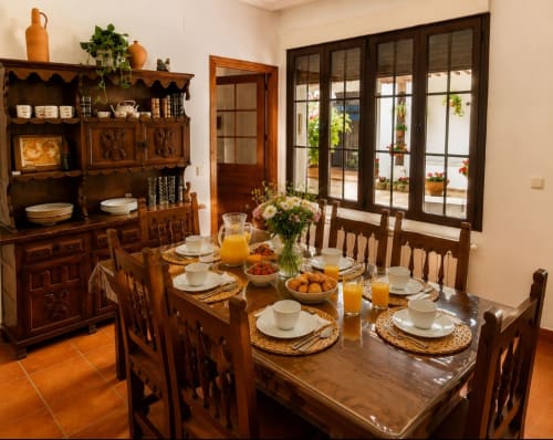 Comedor rústico en Casa Rural La Herrería con mesa de madera, muebles tradicionales, flores frescas y vistas a la terraza