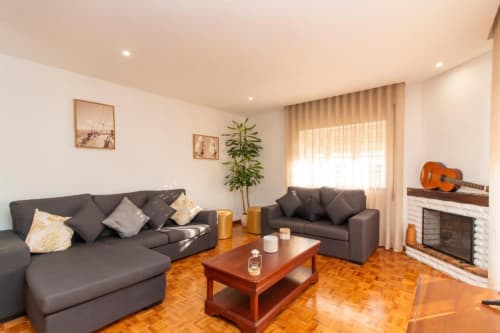 Sala de estar moderna do Sleep & Go hostel em Esposende com sofás cinzentos, mesa de madeira, lareira e guitarra.