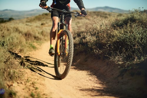 Ciclista de montaña recorriendo sendero desértico cerca de Colmenar de Oreja con montañas al fondo