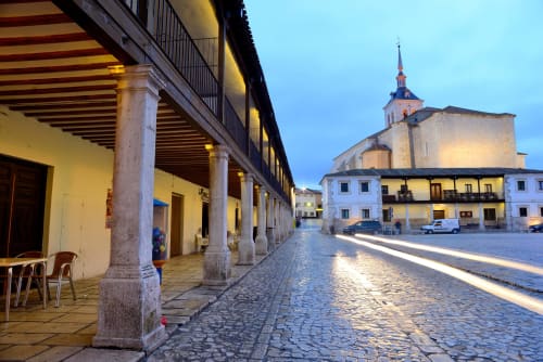 Plaza histórica de Colmenar de Oreja con arcos de piedra, arquitectura tradicional española e iglesia con campanario