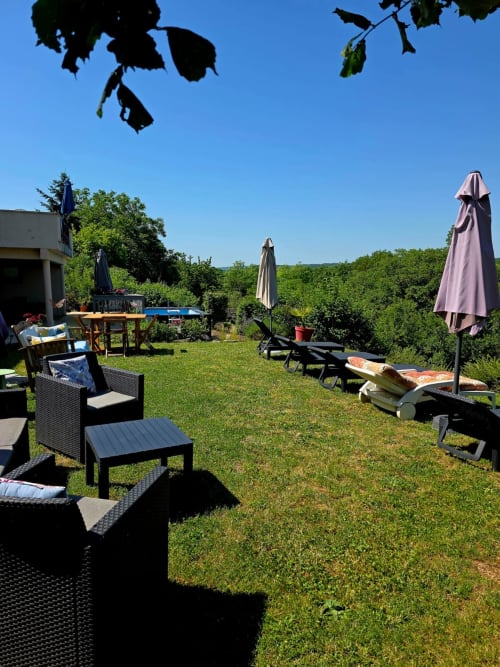 Veranda von La Maison de la Colline mit Liegestühlen, Sonnenschirmen und üppigem Grün in Vers, Frankreich