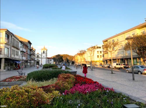 Praça do Sleep & Go hostel em Esposende com canteiros de flores coloridas, igreja histórica e arquitetura ao pôr do sol