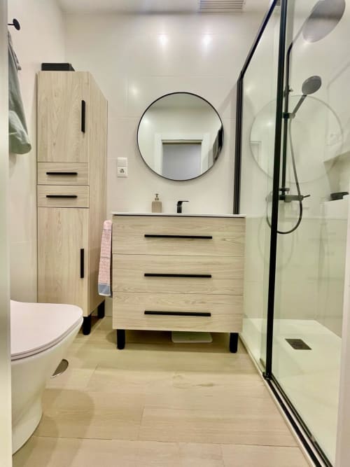 Baño moderno en Solana Urban Lux, Fuengirola, con tocador de madera, espejo redondo y cabina de ducha