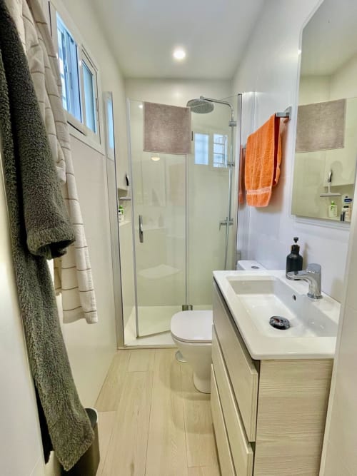 Baño moderno en Solana Urban Lux, Fuengirola, con ducha a ras de suelo, lavabo blanco y suelos de estilo madera