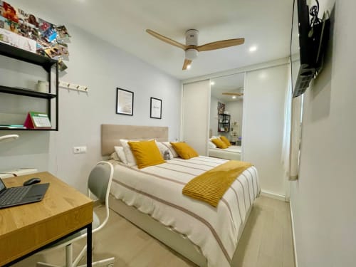 Moderno dormitorio en Solana Urban Lux de Fuengirola con cama, escritorio, acentos amarillos, armario espejo y ventilador de techo