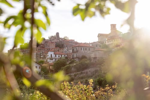 Hôtel Allegria niché dans le village de montagne de Bajardo, Italie, avec ses bâtiments en terre cuite et une végétation luxuriante au premier plan