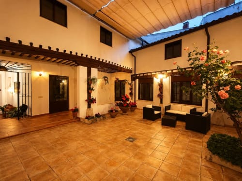 Patio de Casa Rural La Herrería en Colmenar de Oreja con suelo de barro, vigas de madera, plantas en flor y zonas de descanso